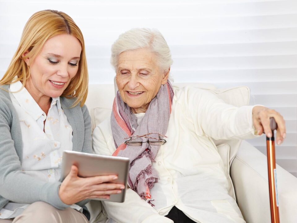 senior lady and adult woman looking on a tablet together while sitting on a couch