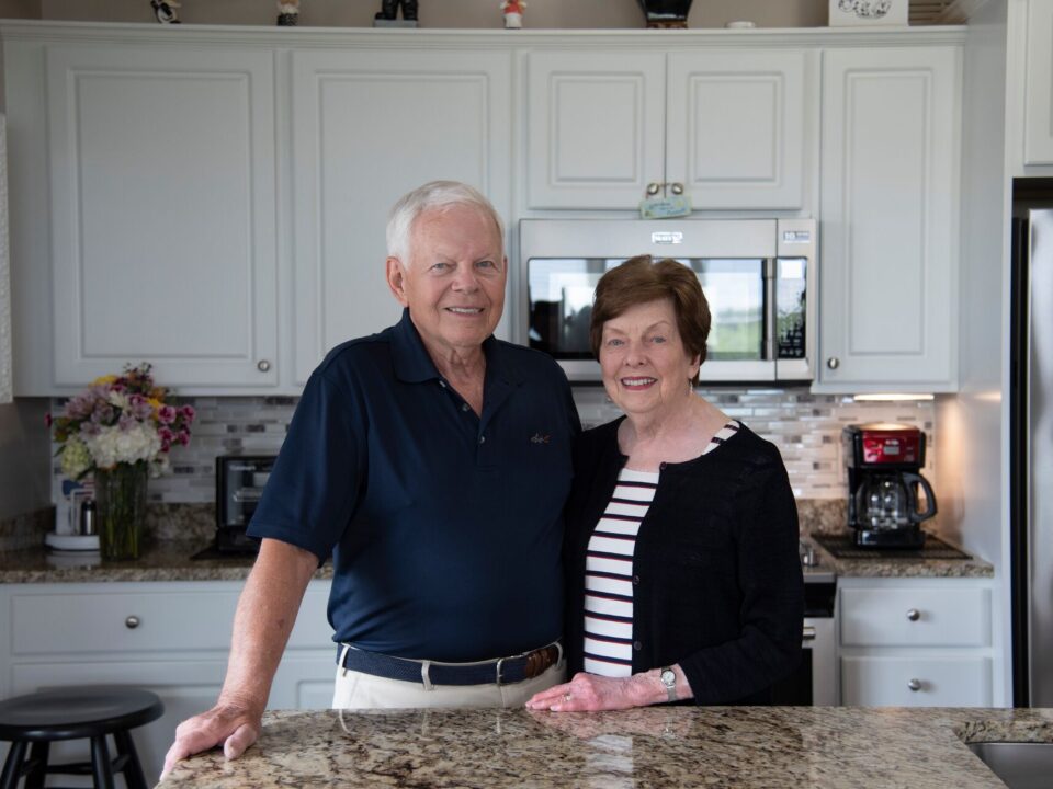 A senior couple stand together in their beautiful senior living apartment kitchen.