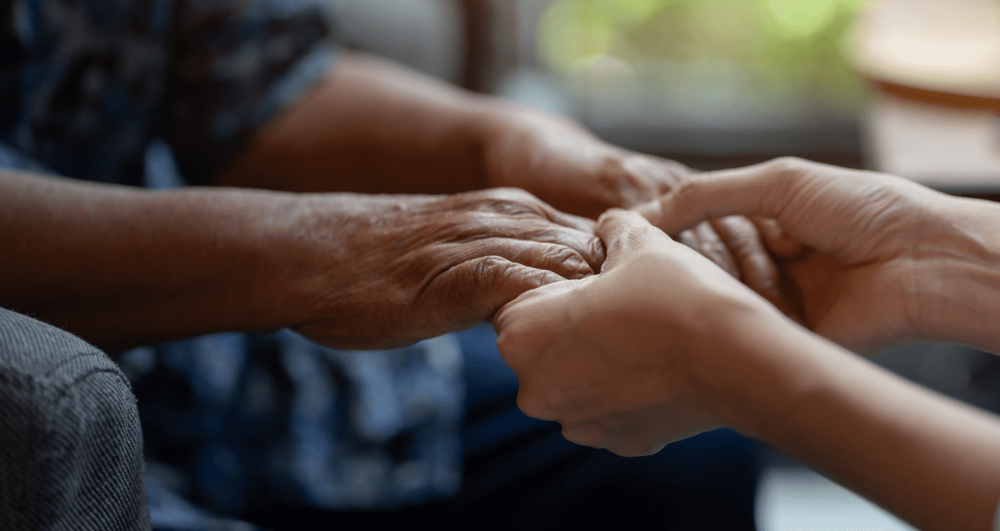 A younger individual holds hands with a Hospice Care resident.