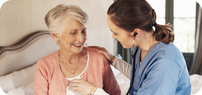 A caregiver using a stethoscope with a smiling community member.