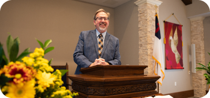 A smiling pastor standing at a pulpit at the Friendship Village chapel.