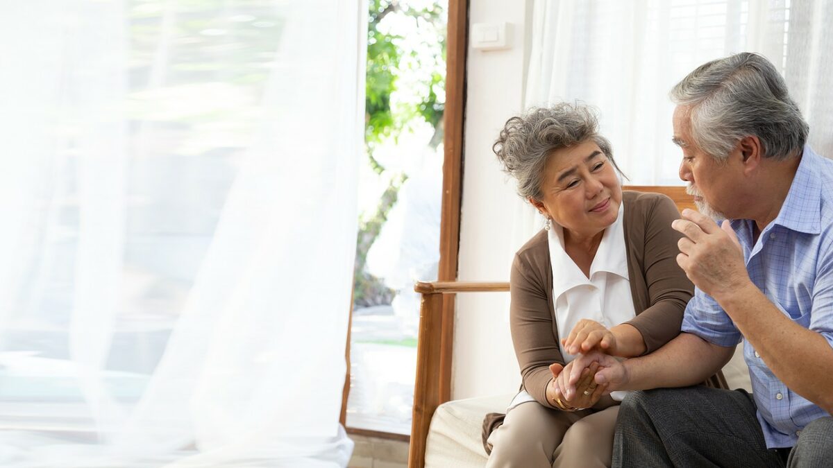 Senior couple talking together on couch, man looks disoriented.