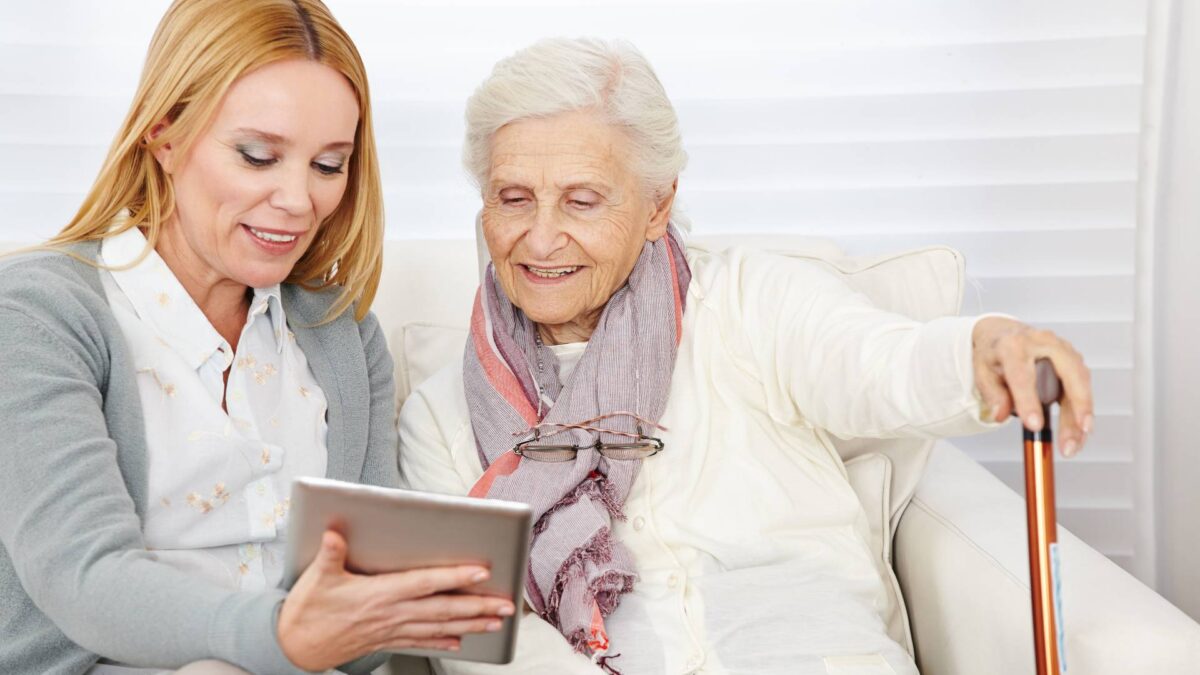 senior lady and adult woman looking on a tablet together while sitting on a couch
