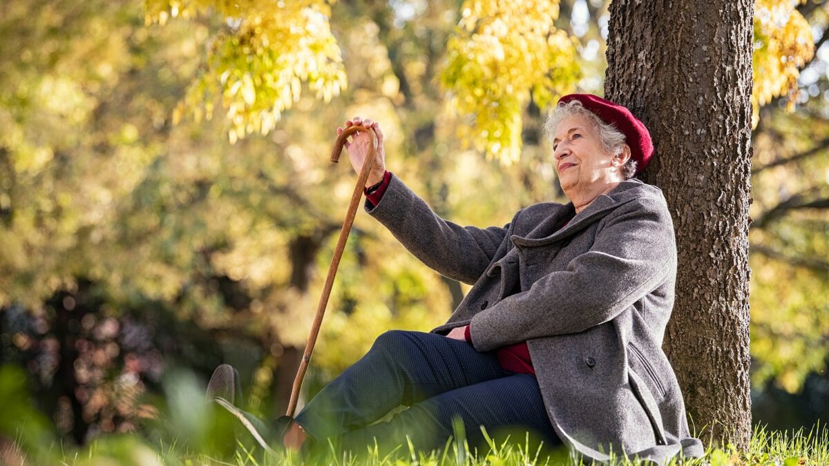 Senior woman sitting and relaxing under a tree in a park.