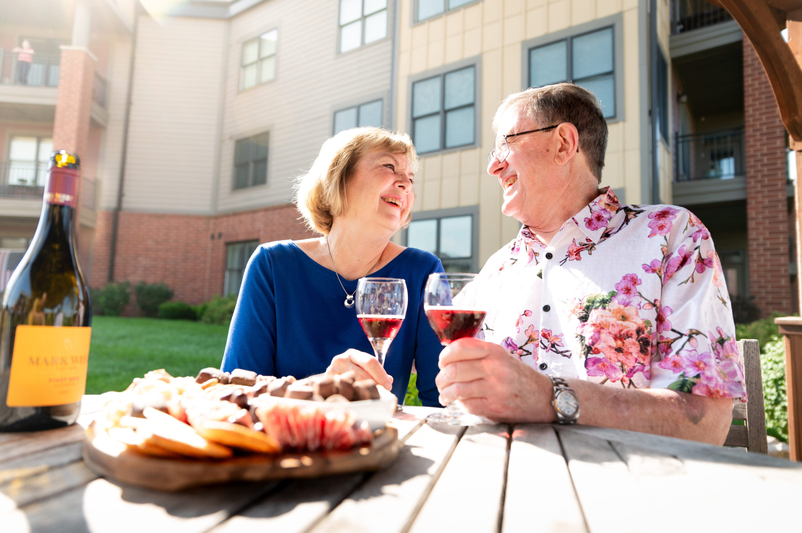 Two community members enjoy glasses of wine and charcuterie in the sunshine.