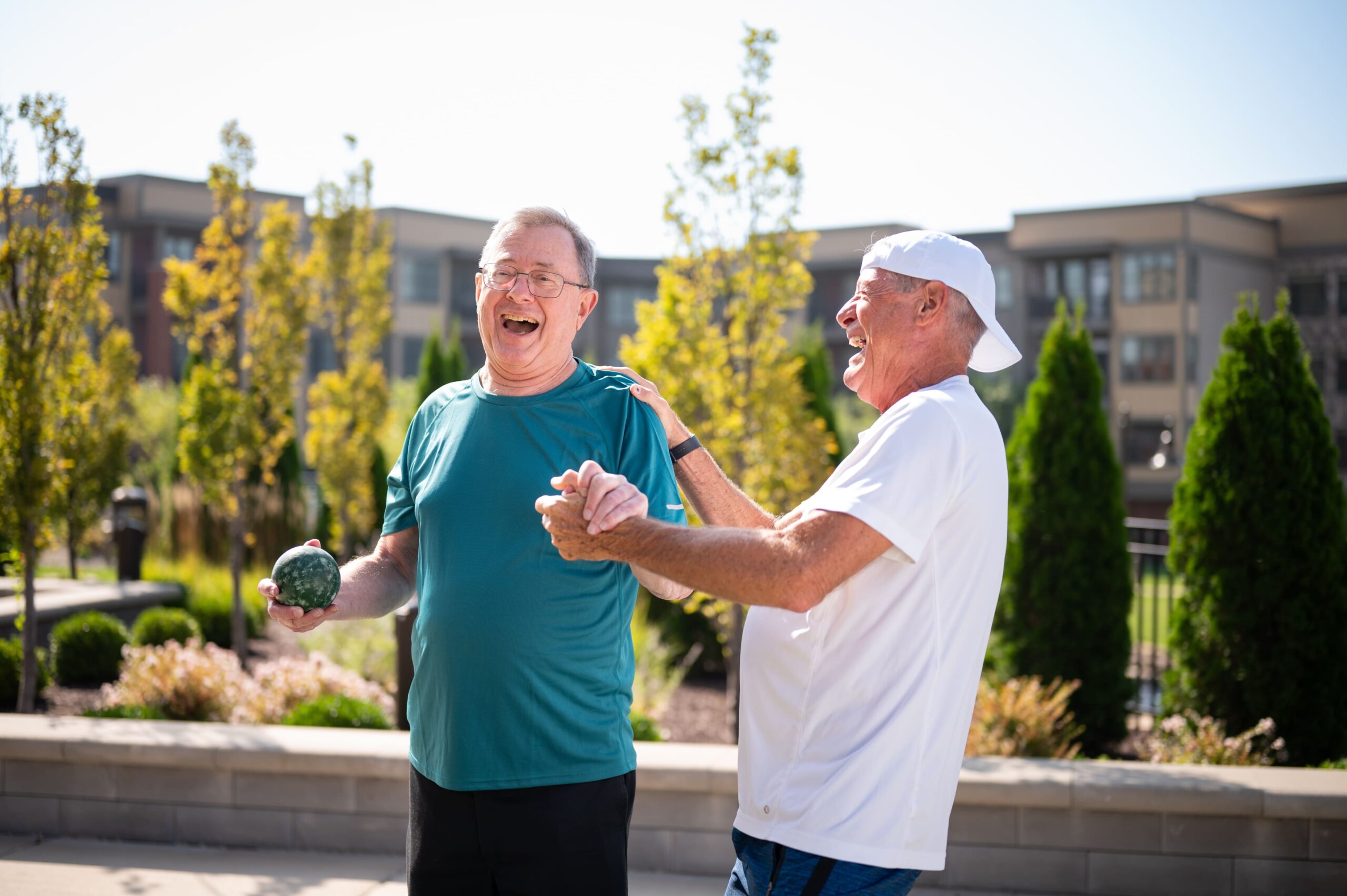 Two community members laugh together while enjoying a game of bocce ball outside.