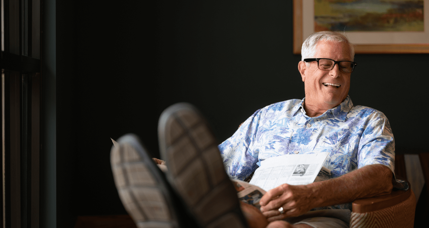 A community member laughing while reclining in a chair with a newspaper.
